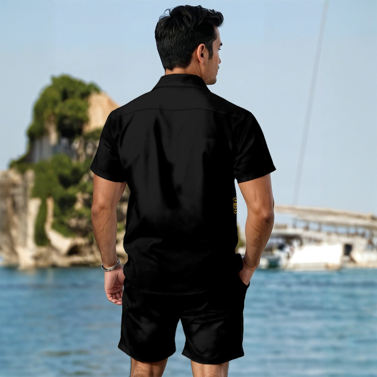 Man wearing a bold print summer tee for men in black standing by the water with greenery in the background